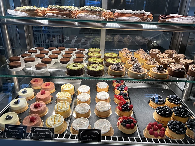Kühlvitrine mit Cheesecakes, Törtchen mit Beeren, Schokoladentörtchen und Pistazienkuchen, oben Éclairs
