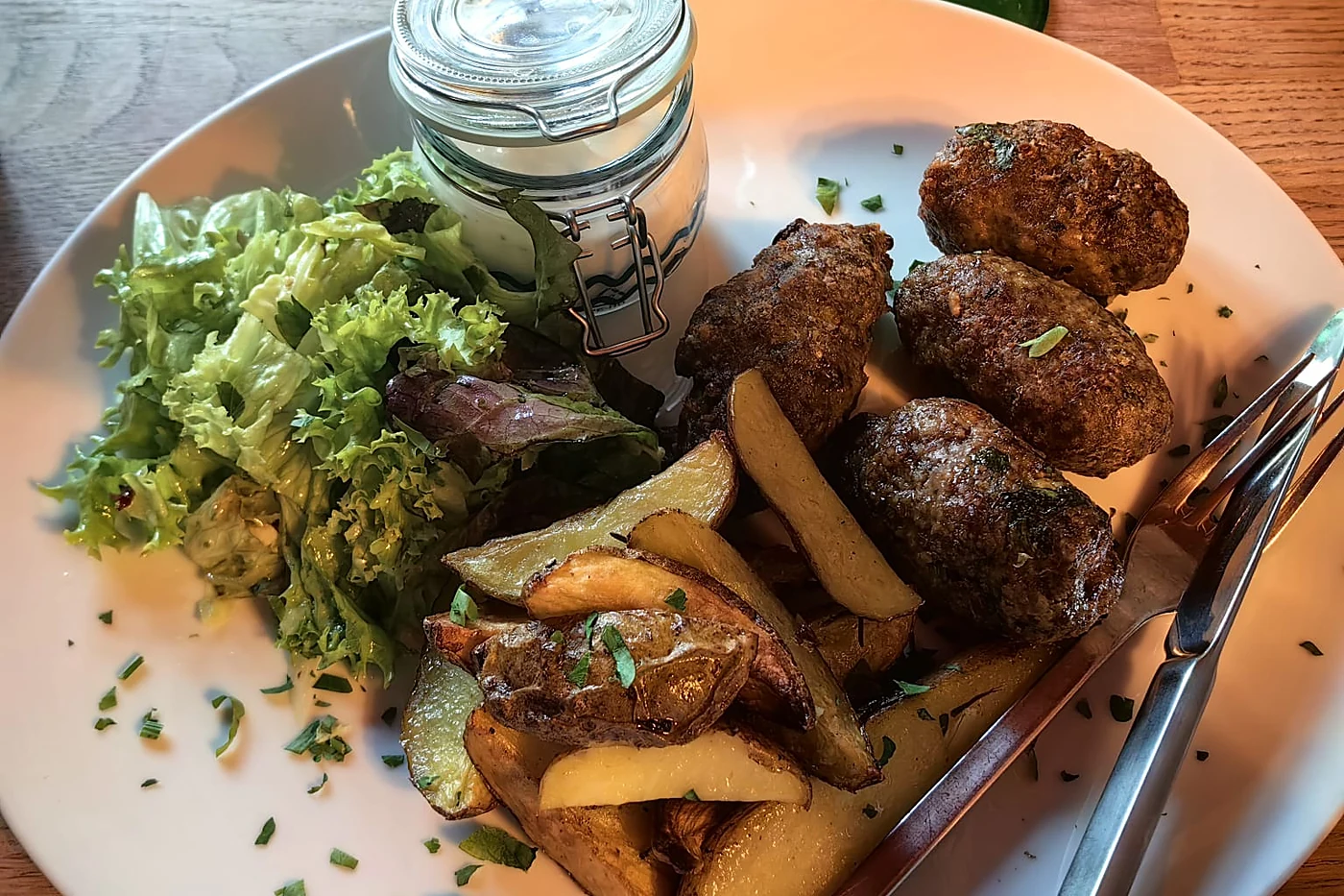 Teller mit Königsberger Klopsen, Kartoffelspalten und Salat im Zum tanzenden Einhorn