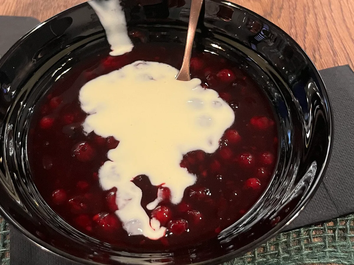 Rote Grütze mit Vanillesauce in einer dunklen Schale