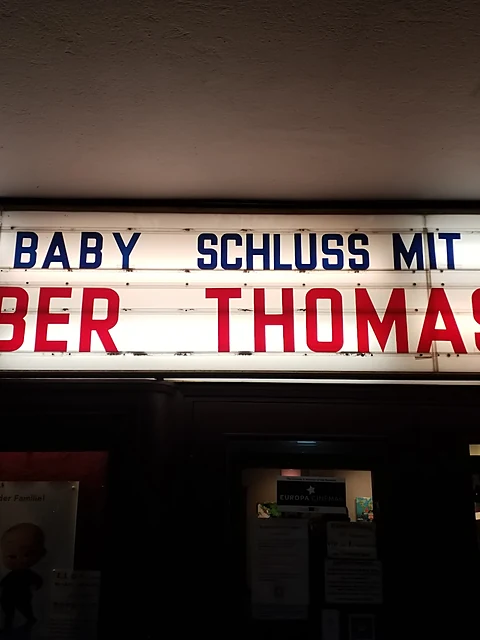Beleuchtete Schaukastentafel über dem Kinoeingang mit aufgesteckten roten und blauen Filmtiteln