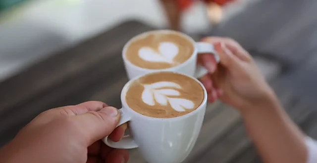 Zwei Hände stoßen mit zwei Cappuccino-Tassen mit Latte-Art an