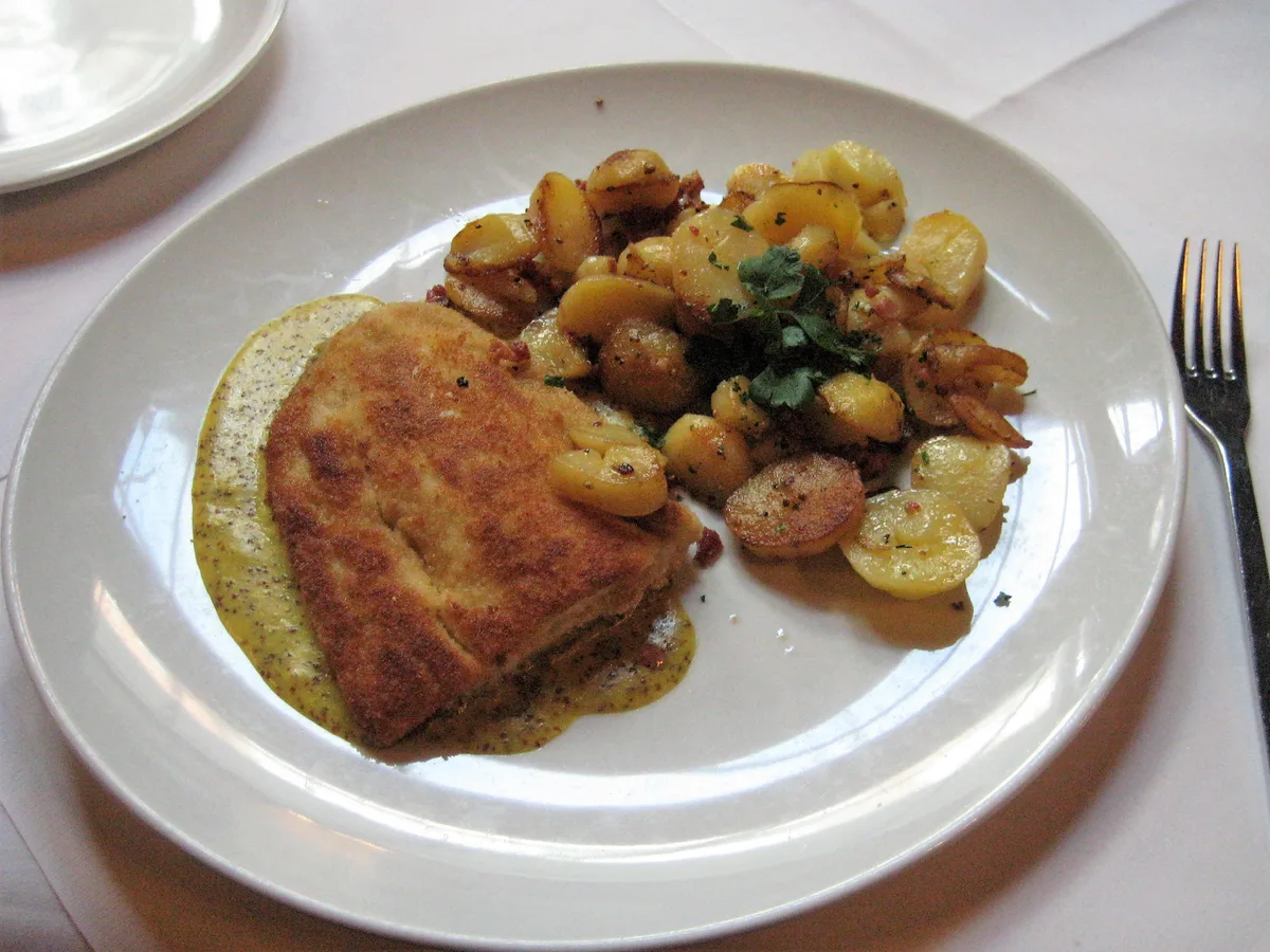 Panierter Fisch mit Senfsauce und Bratkartoffeln auf einem weißen Teller