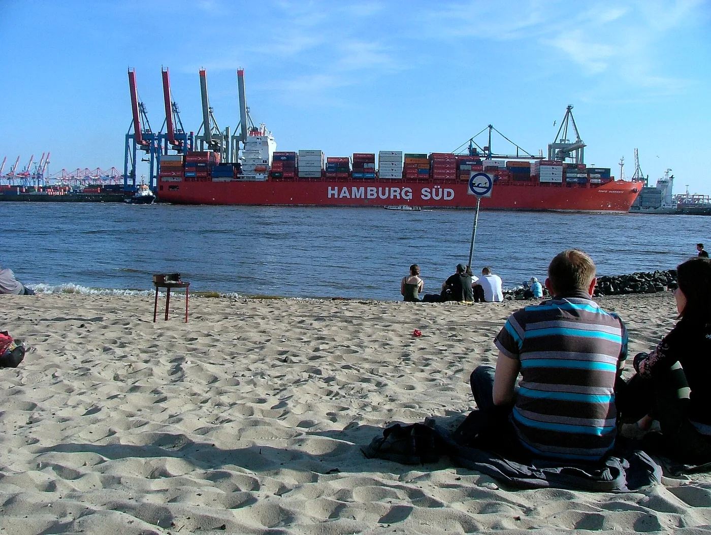 Menschen am Elbstrand in Hamburg vor einem vorbeifahrenden Containerschiff von Hamburg Süd