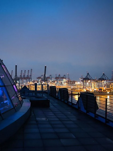 Dachterrasse neben der beleuchteten Glaskuppel der Elbwarte am Abend, dahinter die Lichter der Containerterminals