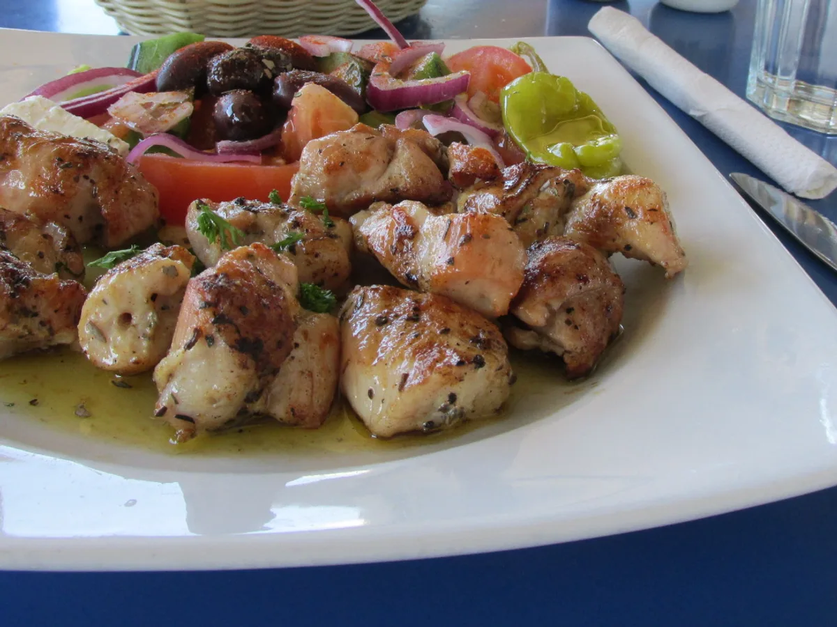 Gegrillte Fleischstücke mit Kräutern und Olivenöl neben Salat auf einem weißen Teller