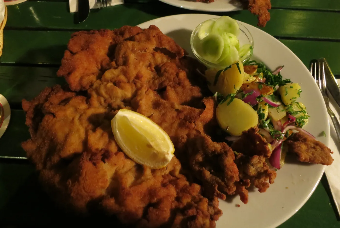 Sehr großes paniertes Schnitzel, das über den Tellerrand hängt, dazu Zitrone und Kartoffelsalat