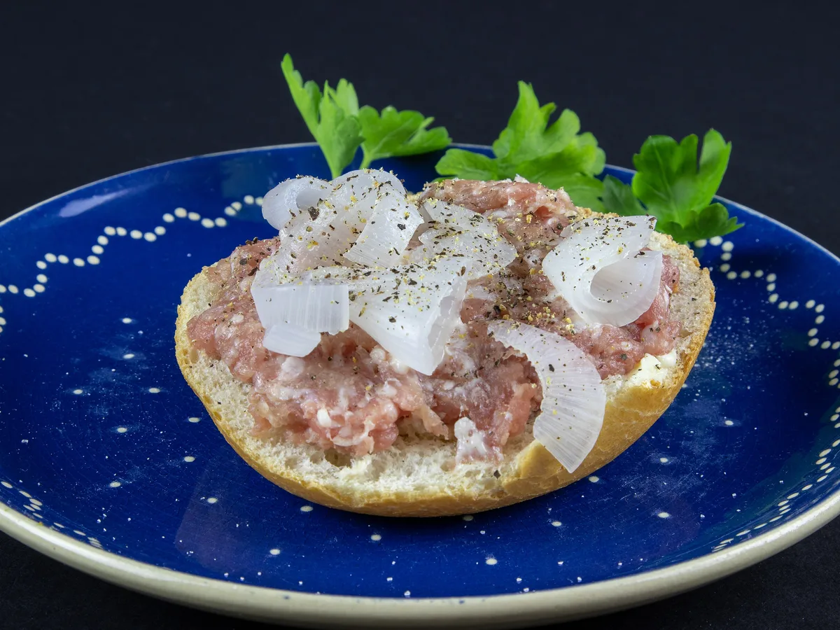 Mettbrötchen mit rohen Zwiebelringen und Pfeffer auf einem blauen Teller