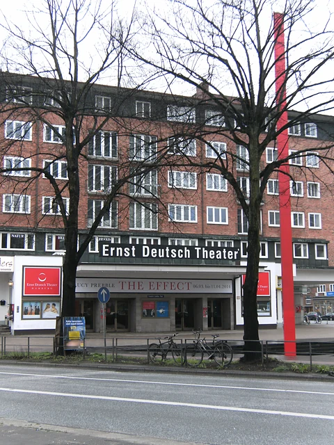 Das Ernst Deutsch Theater hinter kahlen Bäumen, davor die rote Stele