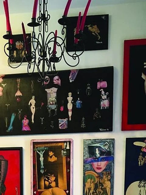 Ausstellungswand mit dicht gehängten, gerahmten erotischen Zeichnungen und Gemälden unter einem schwarzen Kerzenleuchter