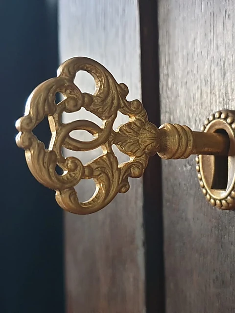 Verzierter goldener Schlüssel steckt im Schloss einer dunklen Holztür