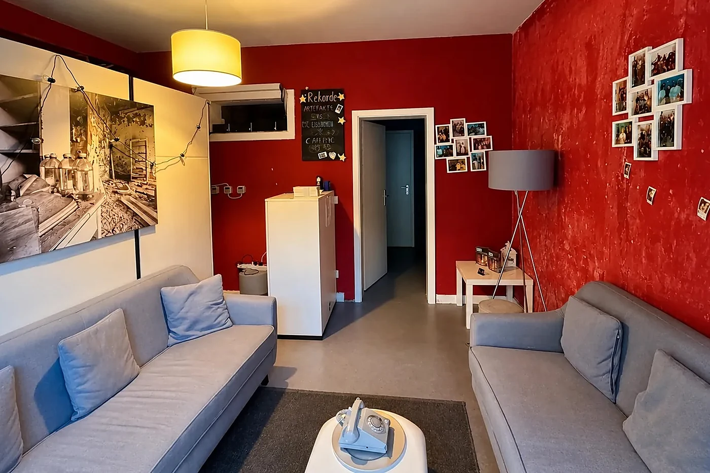 Empfangsraum mit roten Wänden, zwei grauen Sofas, weißem Couchtisch, Fotowand und einem großen Schwarz-Weiß-Foto
