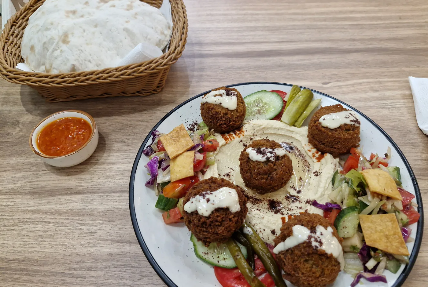 Falafelteller mit Hummus, Salat, eingelegtem Gemüse und Fladenbrot auf einem hellen Teller