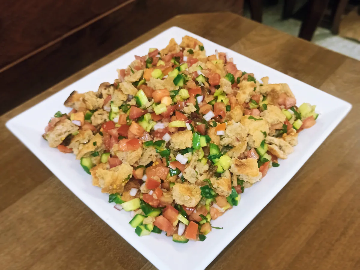 Fattouchsalat mit Tomaten, Gurken, Frühlingszwiebeln und gerösteten Brotstücken auf einem weißen Teller