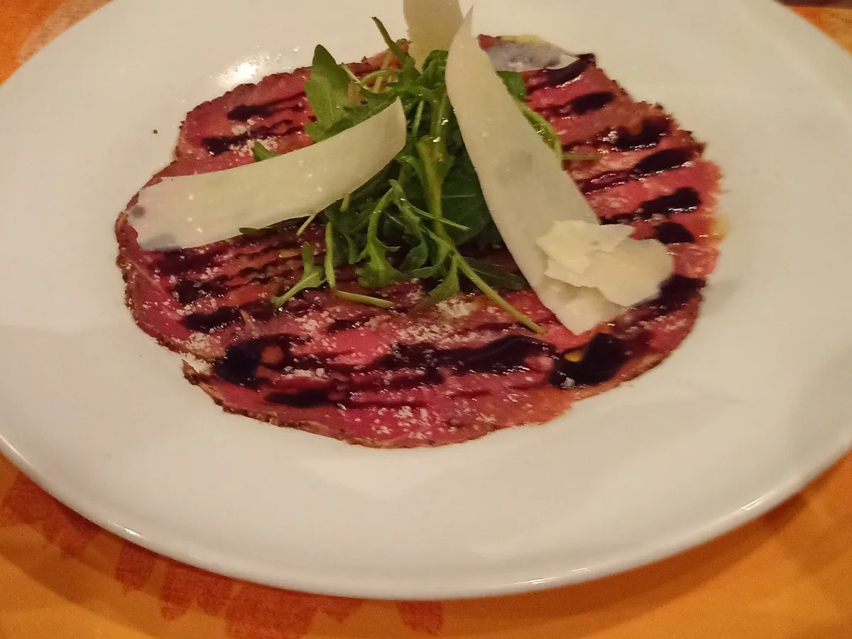 Rindercarpaccio mit Rucola, Parmesanspänen und Balsamico auf einem weißen Teller