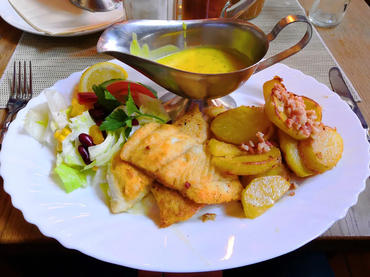 Pannfisch mit Bratkartoffeln, Senfsauce, Zitrone und Dill auf einem weißen Teller