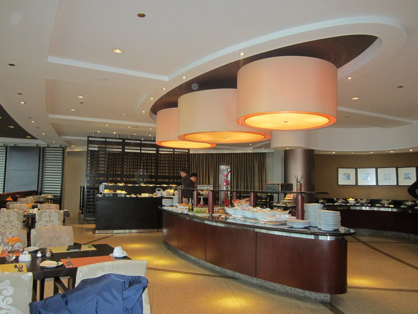 Geschwungener Buffettresen in einem Hotelrestaurant mit Tellern, Obst und gedeckten Tischen