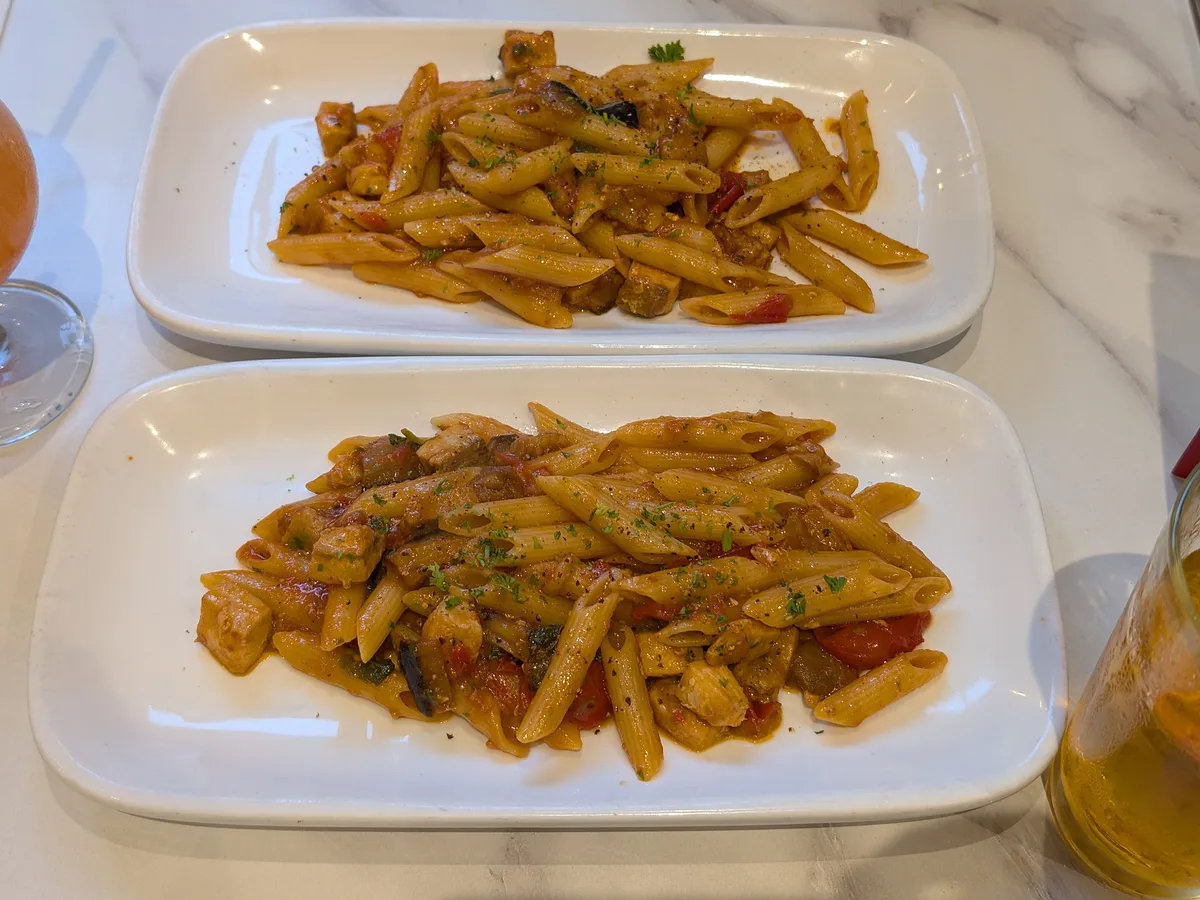 Penne mit Tomatensauce, Gemüse und Kräutern auf einem länglichen weißen Teller