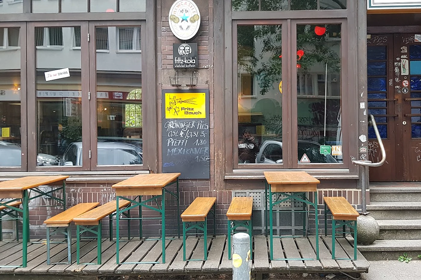 Fassade des Fritz Bauch mit Bierbänken auf dem Gehweg, gelbem Schild und Kreidetafel mit Bierpreisen