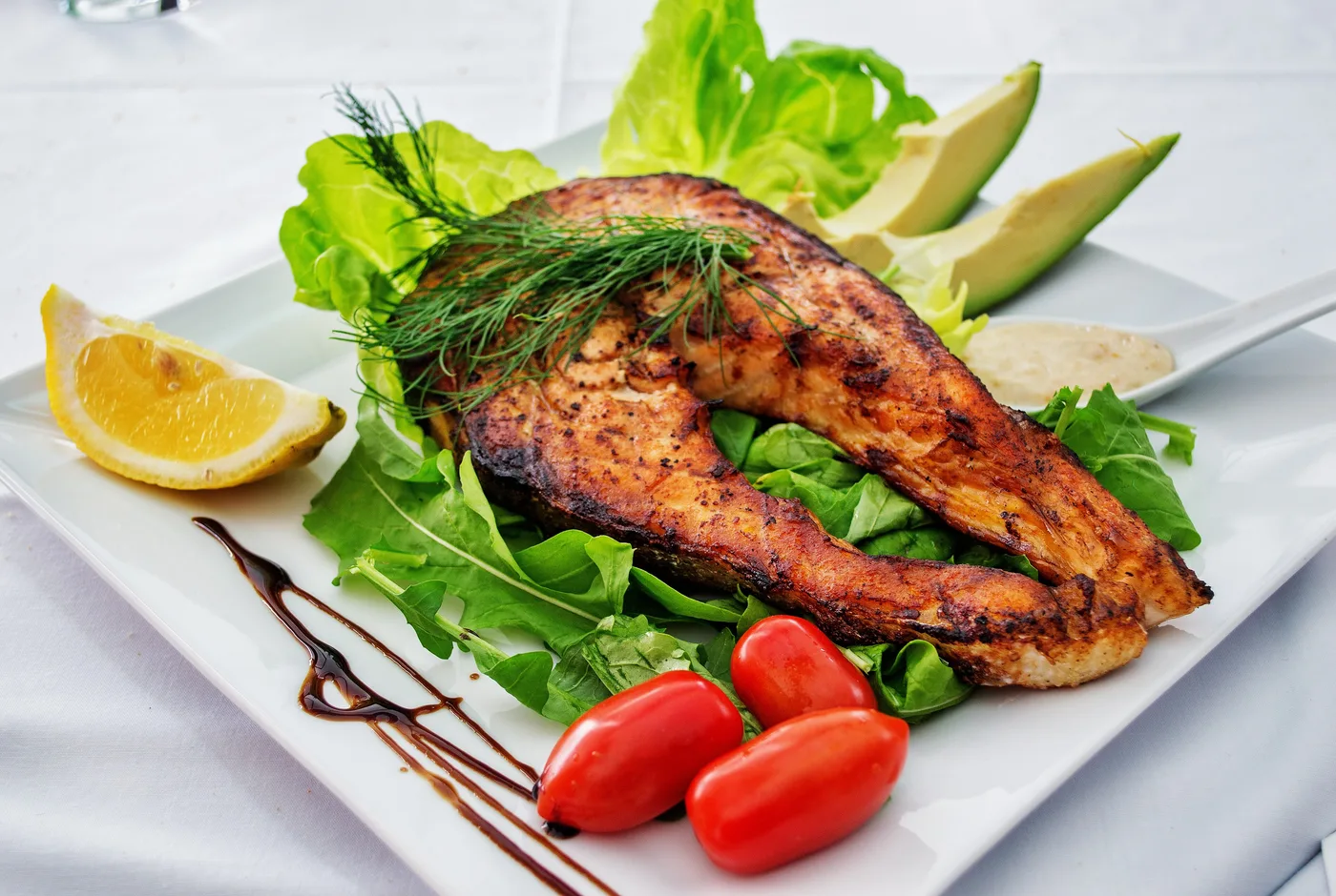 Gegrilltes Lachsfilet mit Salat, Zitrone und Tomaten auf einem weißen Teller
