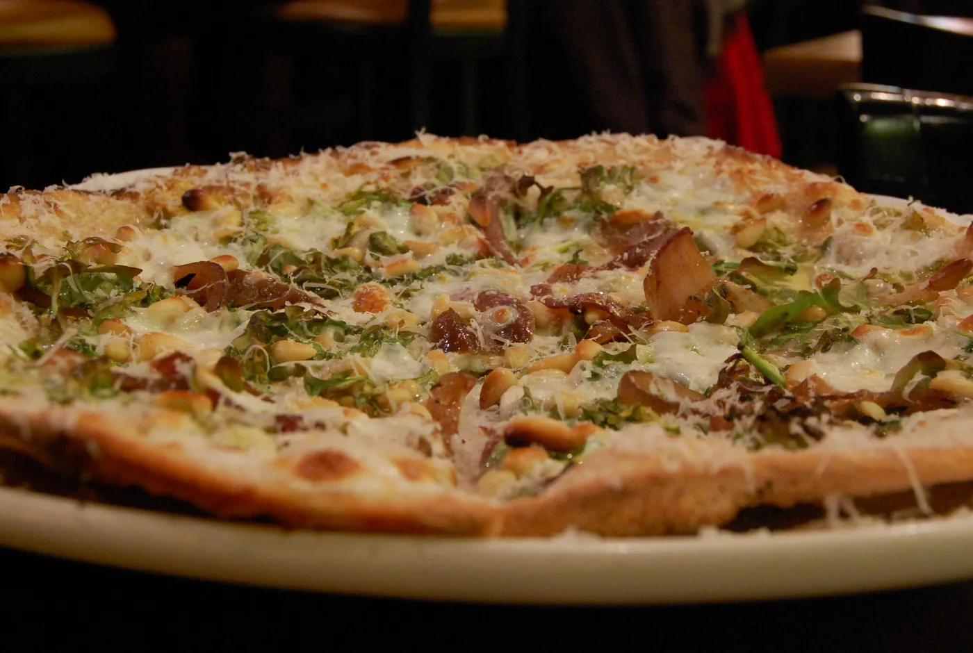 Dünne Pizza mit Rucola, geriebenem Käse und Pinienkernen auf einem hellen Teller