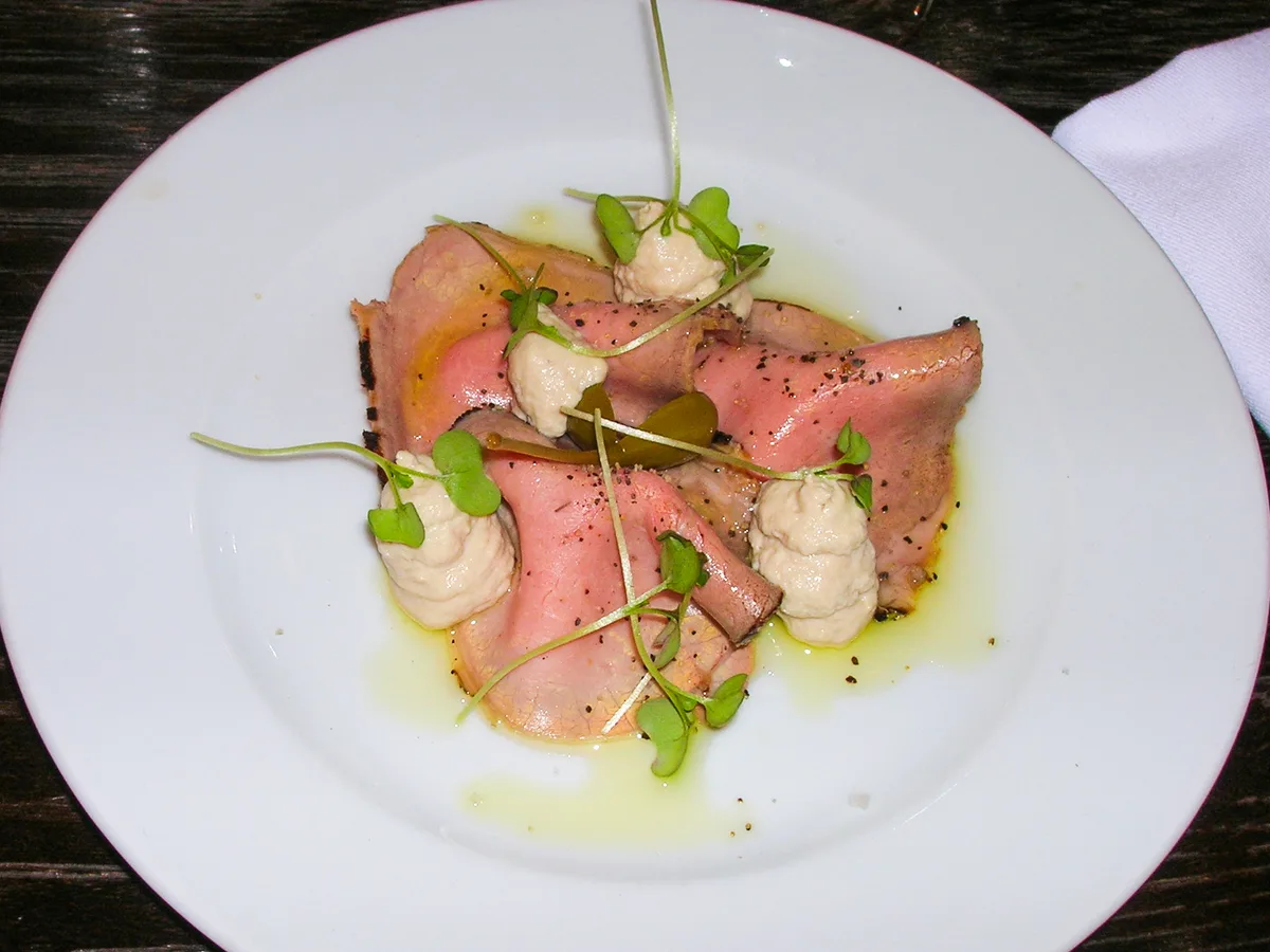 Vitello tonnato mit dünnen Kalbfleischscheiben, Thunfischcreme, Kapern und Kresse auf einem weißen Teller