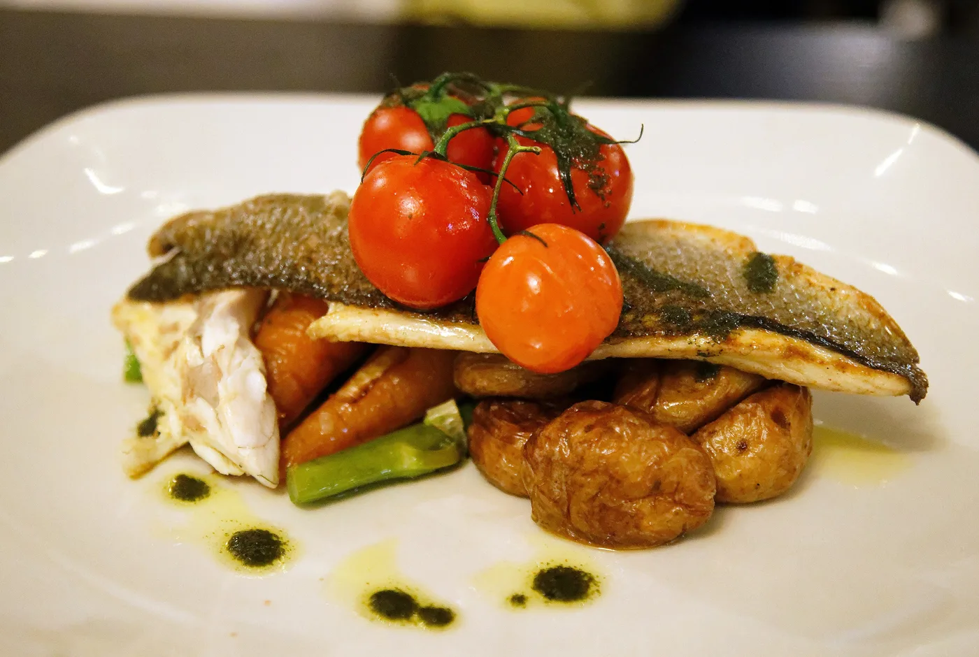 Gebratenes Fischfilet mit Kirschtomaten, Karotten, Zuckerschoten und kleinen Bratkartoffeln auf einem weißen Teller