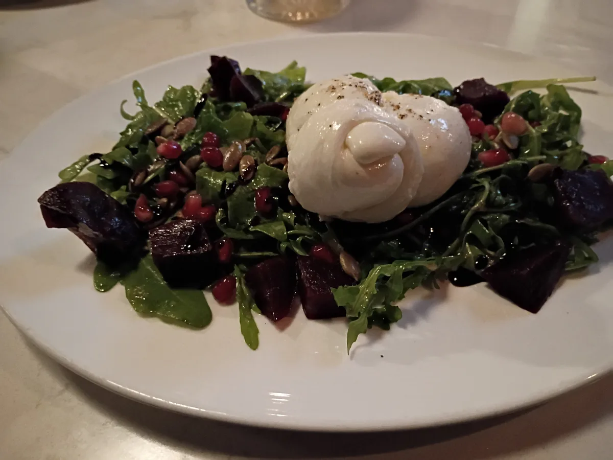 Burrata auf Rucola mit Roter Bete, Granatapfelkernen und Kernen auf einem weißen Teller