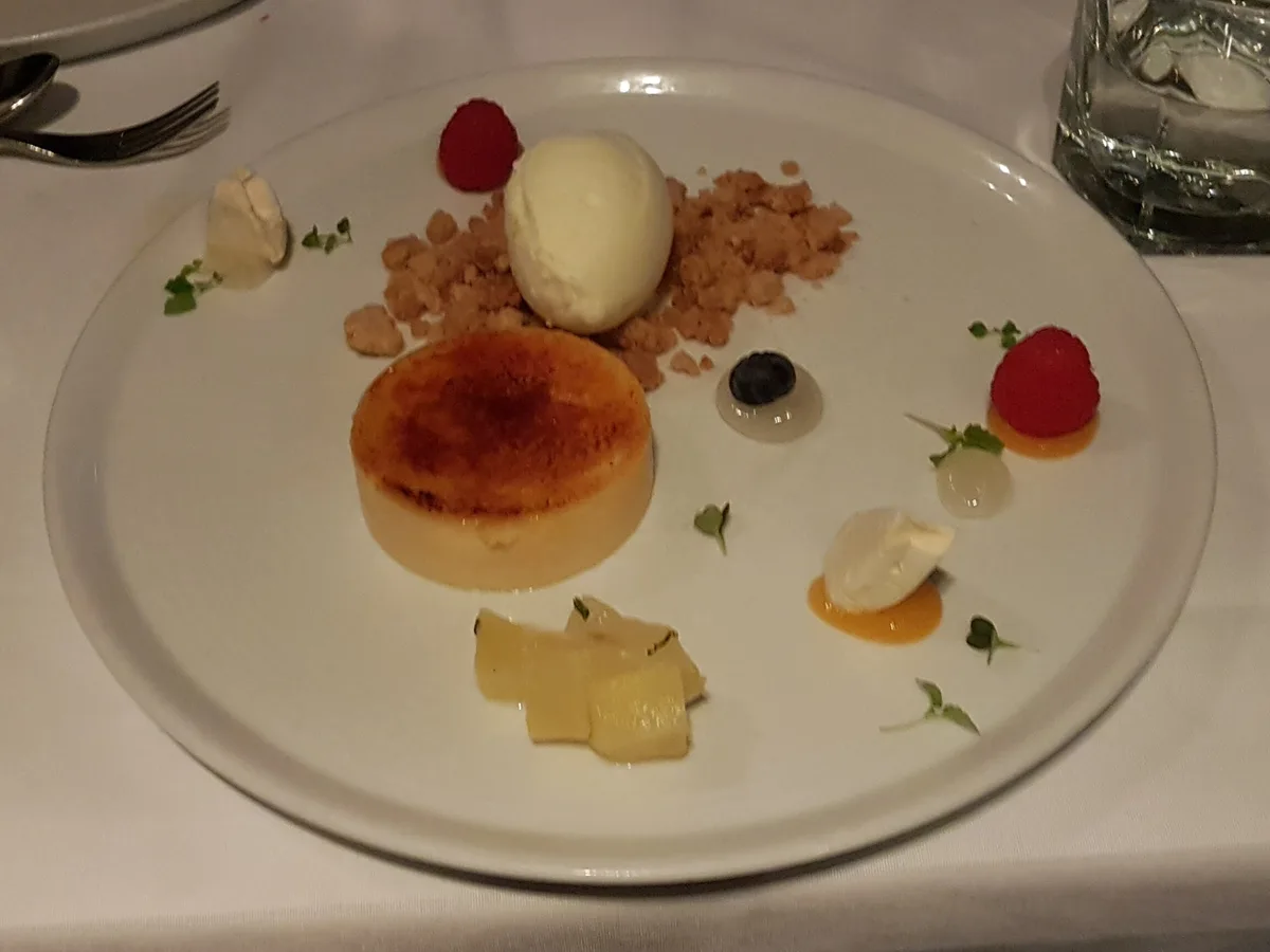 Crème brûlée mit einer Nocke Eis, Streuseln, Himbeeren und Fruchtspiegeln auf einem weißen Teller