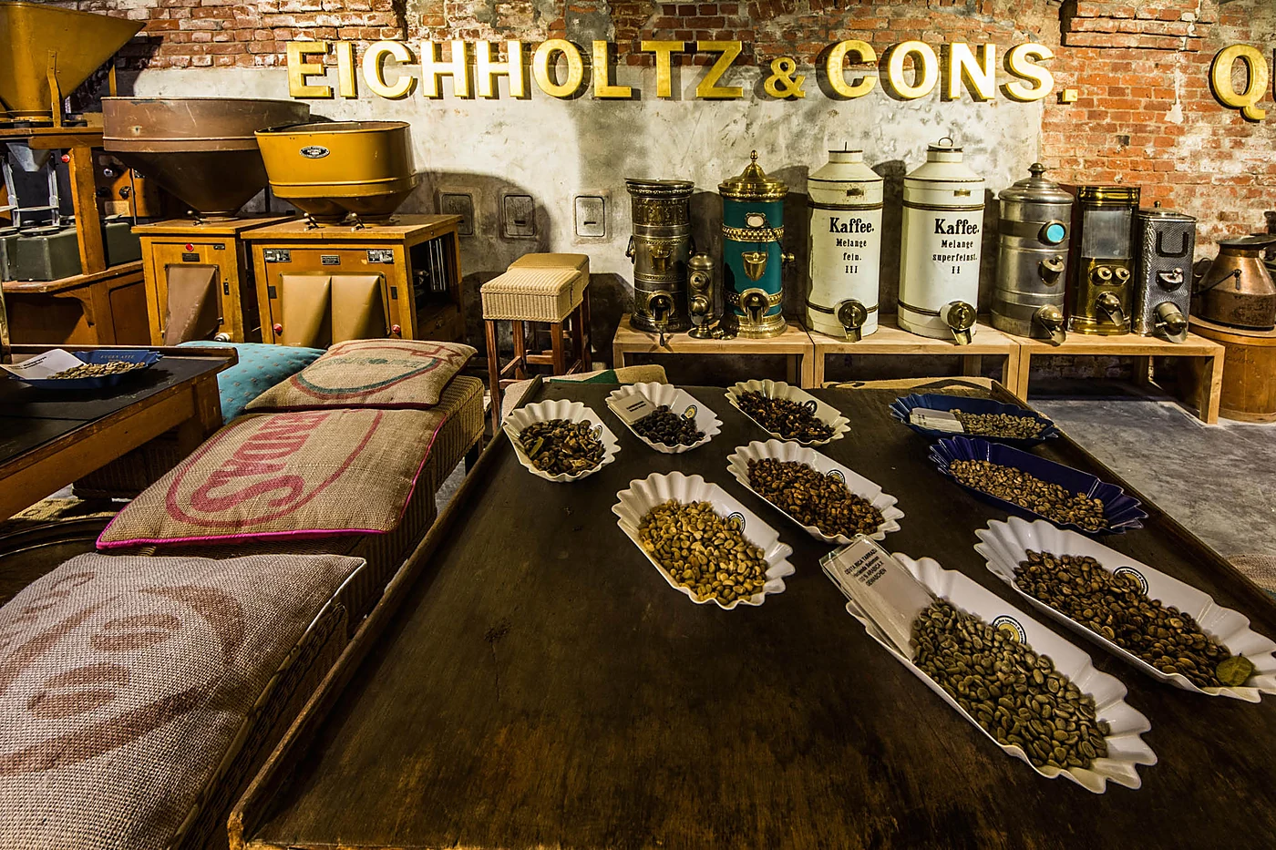 Ausstellungsraum des Kaffeemuseums mit Schriftzug „Eichholtz & Cons.“ an der Backsteinwand, Vorratsdosen, Kaffeesäcken und Schalen mit Rohkaffee
