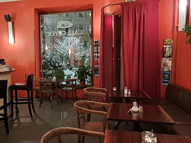 Gastraum mit roten Wänden, Holztischen, Stühlen und Blick auf das Fenster mit dem Schriftzug Café Geyer