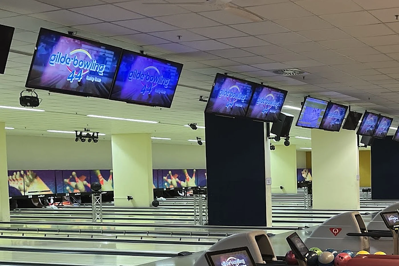 Reihe von Bowlingbahnen mit Bildschirmen unter der Decke, auf denen das Logo gilde-bowling 44 leuchtet