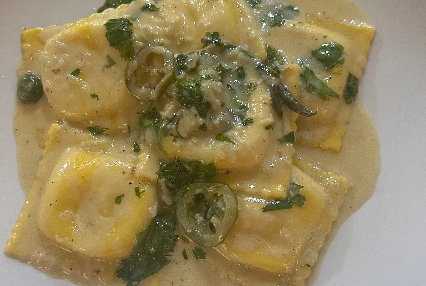Ravioli in heller Rahmsauce mit Kräutern und Salbeiblättern in einem weißen Teller