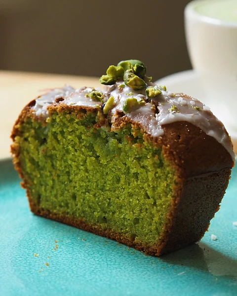 Angeschnittener grüner Matcha-Pistazien-Kastenkuchen mit Zuckerglasur und Pistazien auf türkisfarbenem Teller