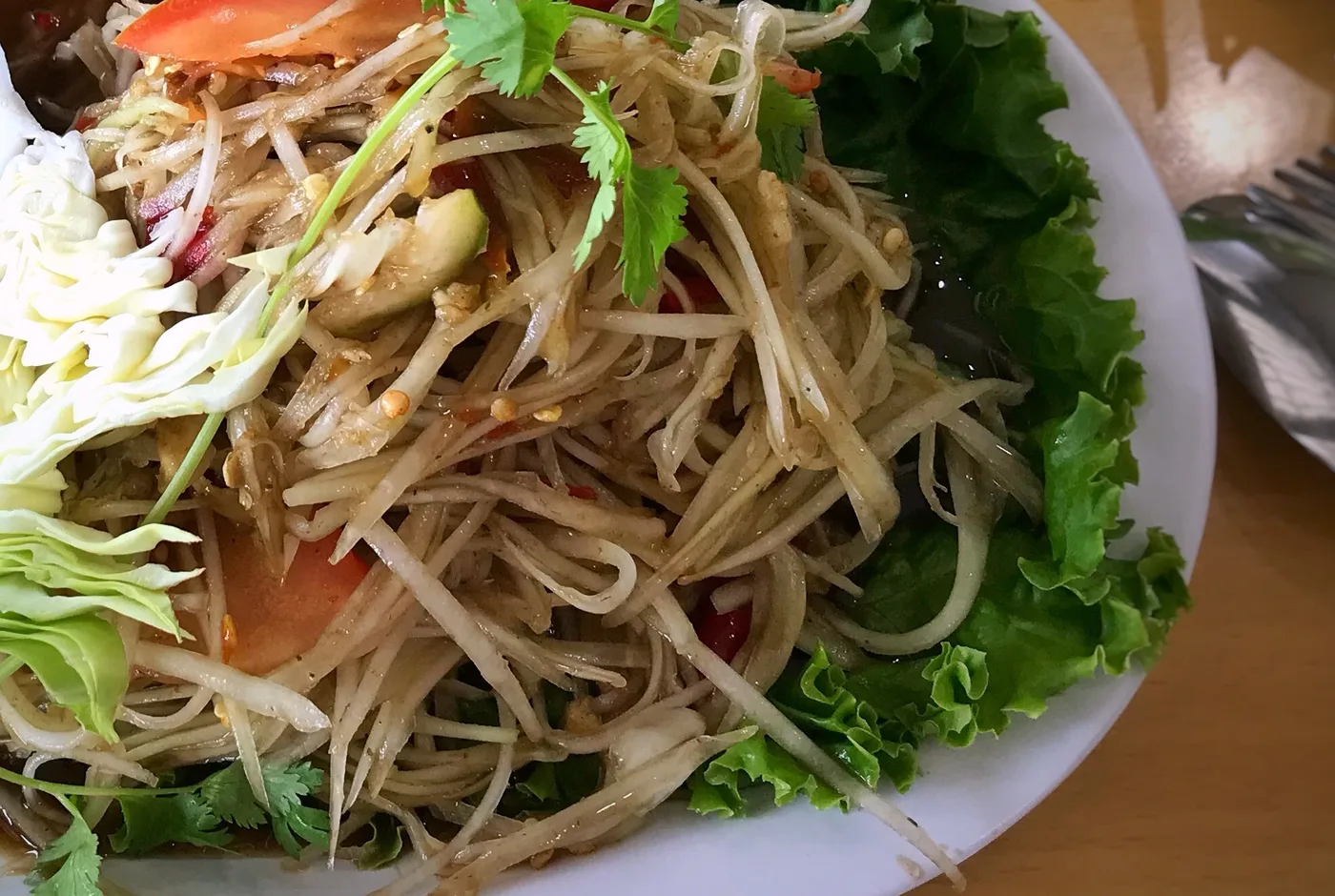 Salat aus geraspelter grüner Papaya mit Tomate, Kohl, Koriander und Salatblättern auf einem weißen Teller