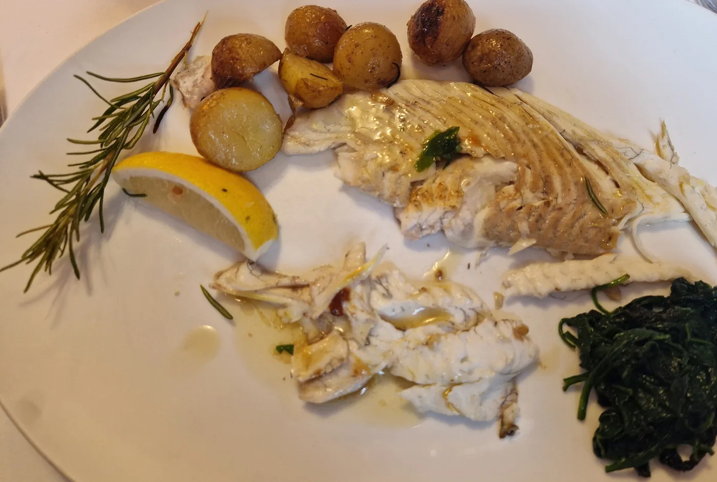 Filetierter Plattfisch mit Rosmarin, Zitrone, kleinen Kartoffeln und Blattspinat auf einem weißen Teller