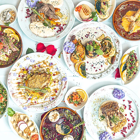 Viele Teller und Schälchen mit libanesischen Mezza von oben: Hummus, Salate, Fleischgerichte, Granatapfelkerne und Blüten