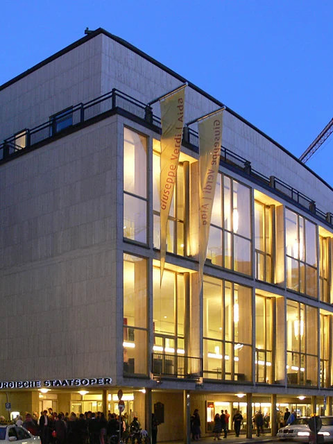 Die Staatsoper bei Nacht, beleuchtete Foyers hinter der Glasfront und der Schriftzug Staatsoper