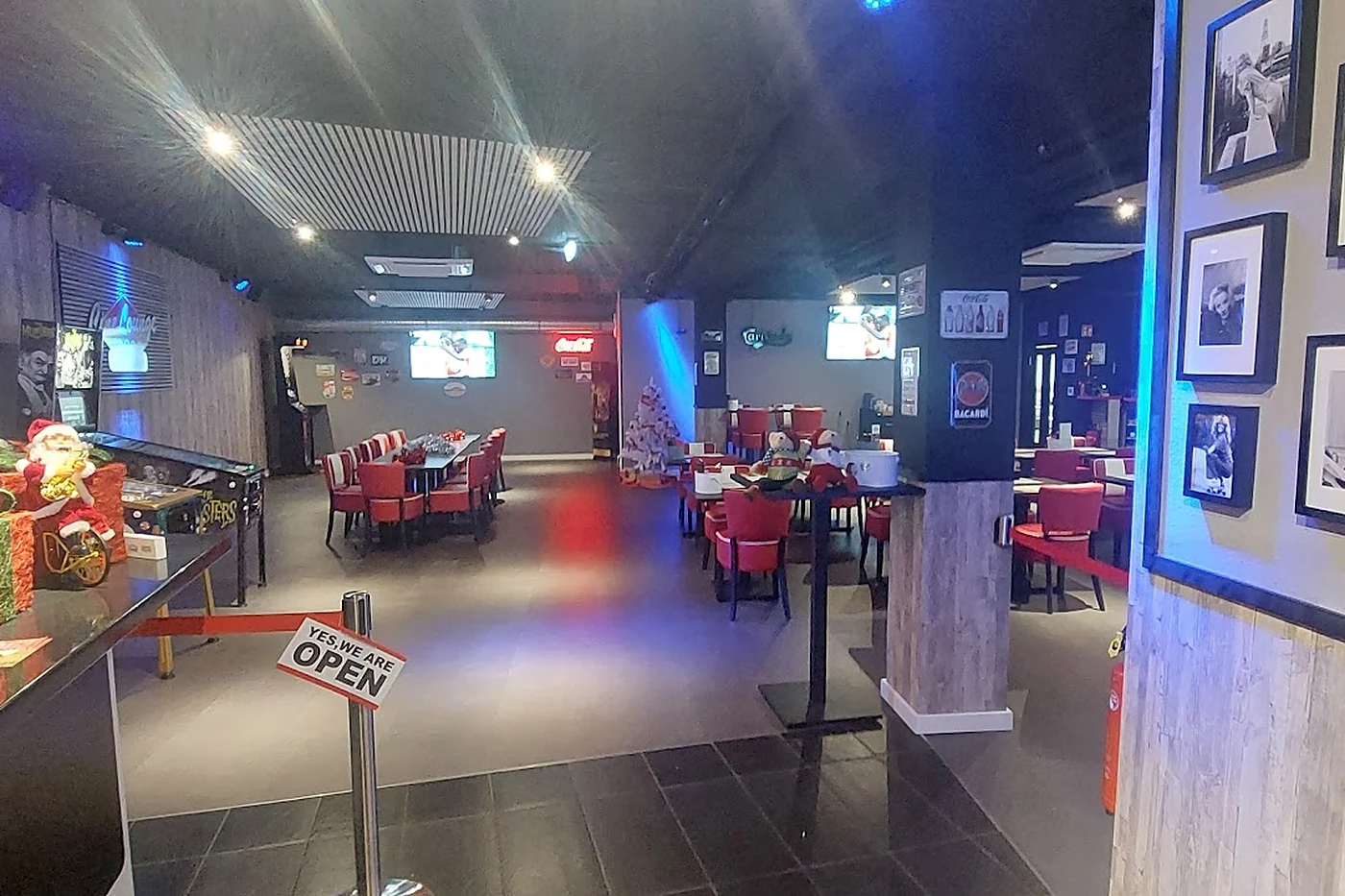 Diner mit roten Stühlen, langen Tischen, Bildschirmen an der Wand und blauem Licht unter der Decke