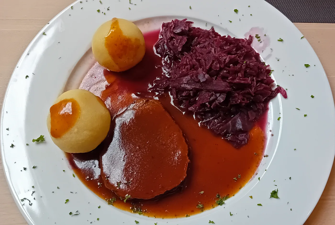 Rinderbraten in dunkler Sauce mit zwei Kartoffelklößen und Rotkohl auf einem weißen Teller