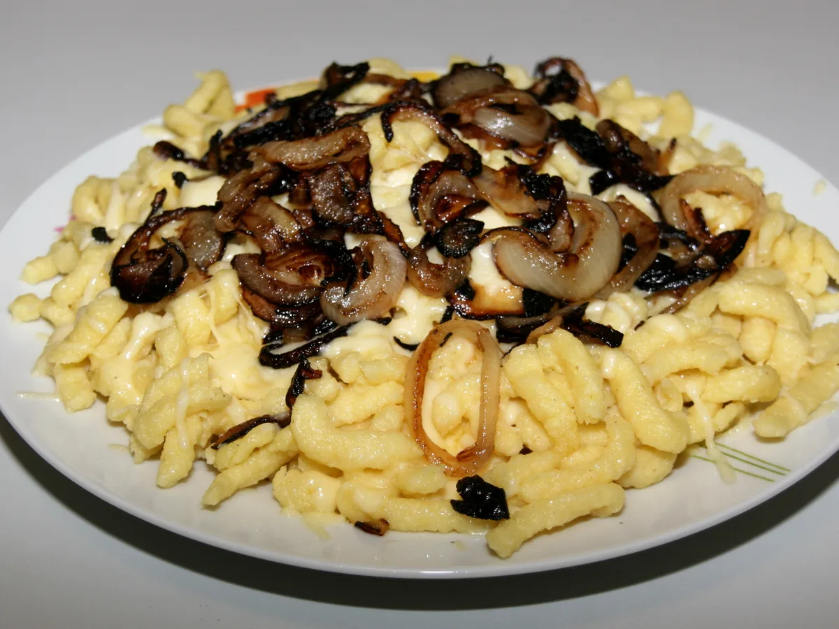Käsespätzle mit geschmolzenem Käse und gerösteten Zwiebelringen auf einem weißen Teller