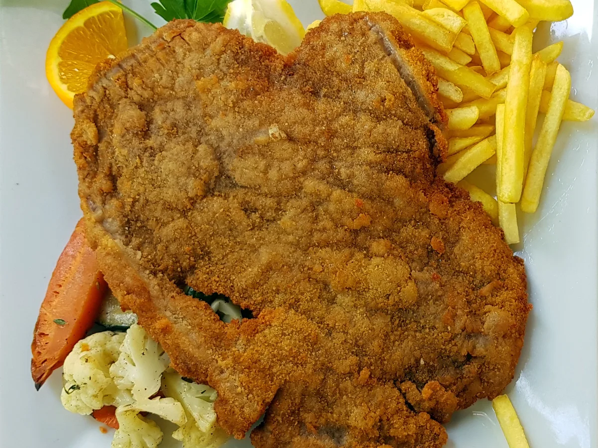 Paniertes Schnitzel mit Pommes frites, Zitrone, Tomate und Blumenkohl auf einem weißen Teller