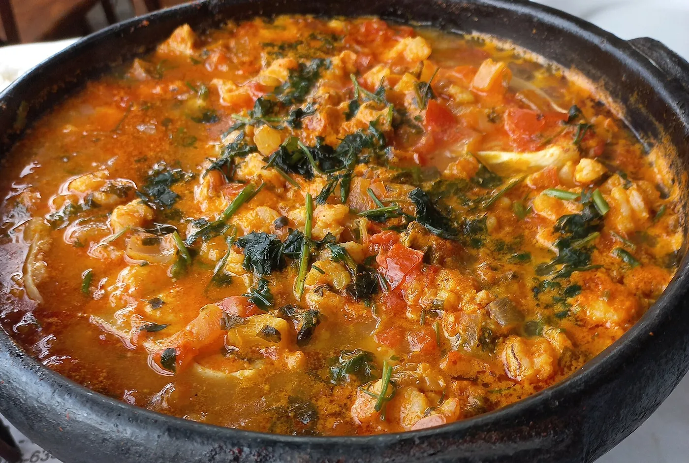 Moqueca mit Fisch, Tomaten, Zwiebeln und Koriander in einem schwarzen Tontopf