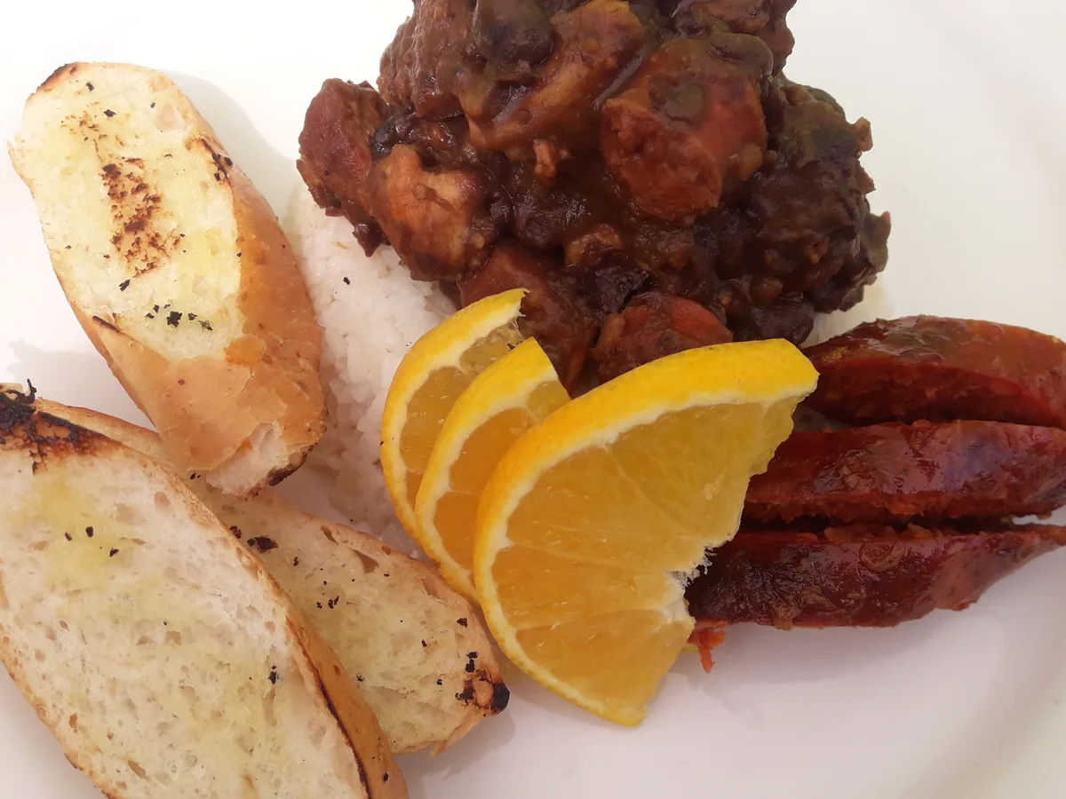Feijoada mit schwarzen Bohnen und Fleisch, dazu Reis, geröstetes Weißbrot, Orangenspalten und Wurst auf einem weißen Tel