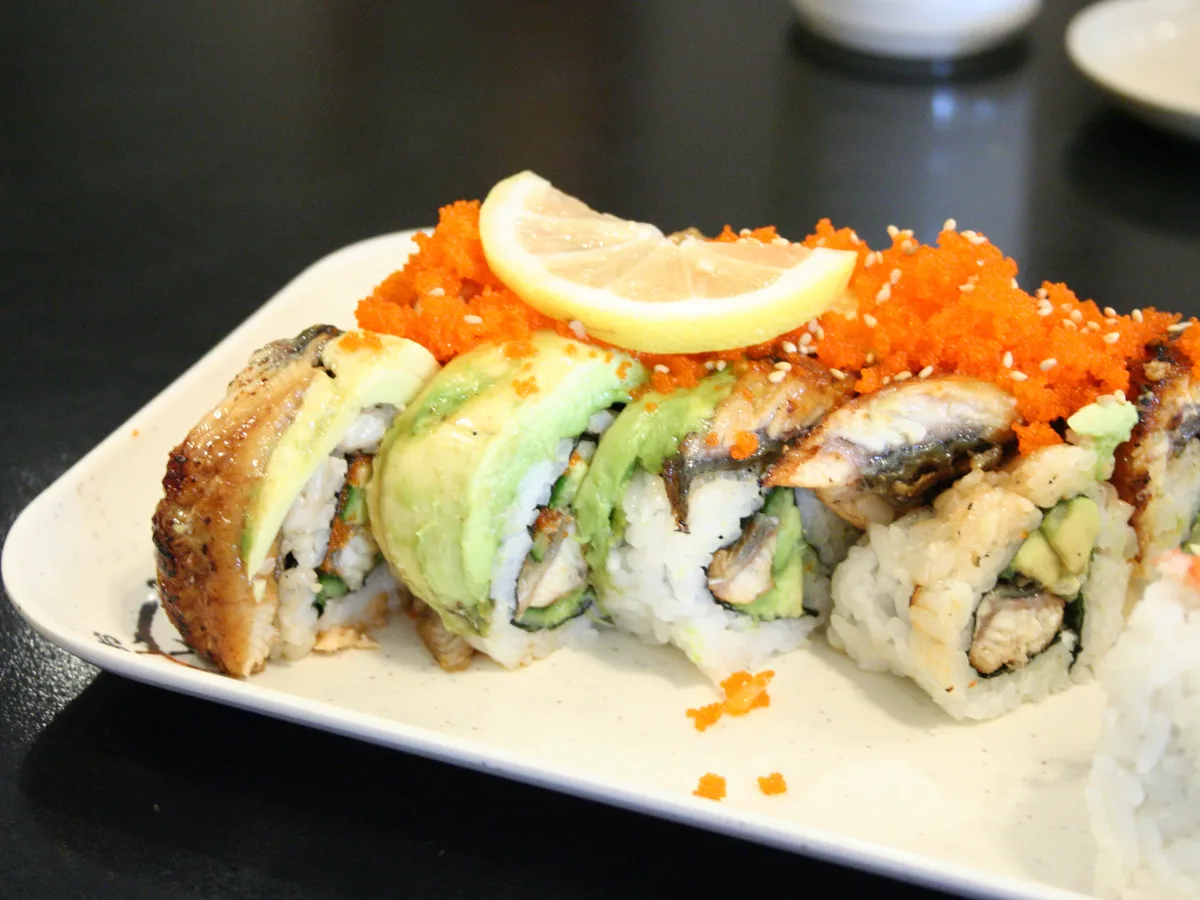 Inside-out-Roll mit Aal, Avocado und orangefarbenem Fischrogen auf einem hellen Teller