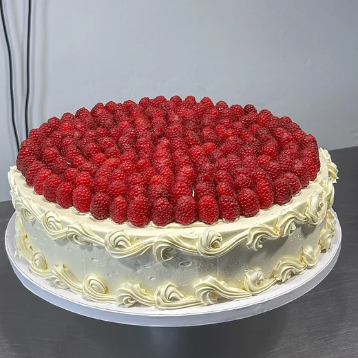 Runde Torte, dicht mit frischen Himbeeren belegt, mit gespritztem Sahnerand