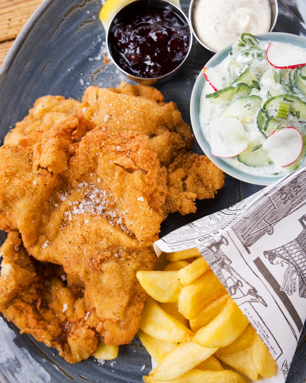 Wiener Schnitzel mit Pommes, Preiselbeeren und Gurkensalat auf blauem Teller