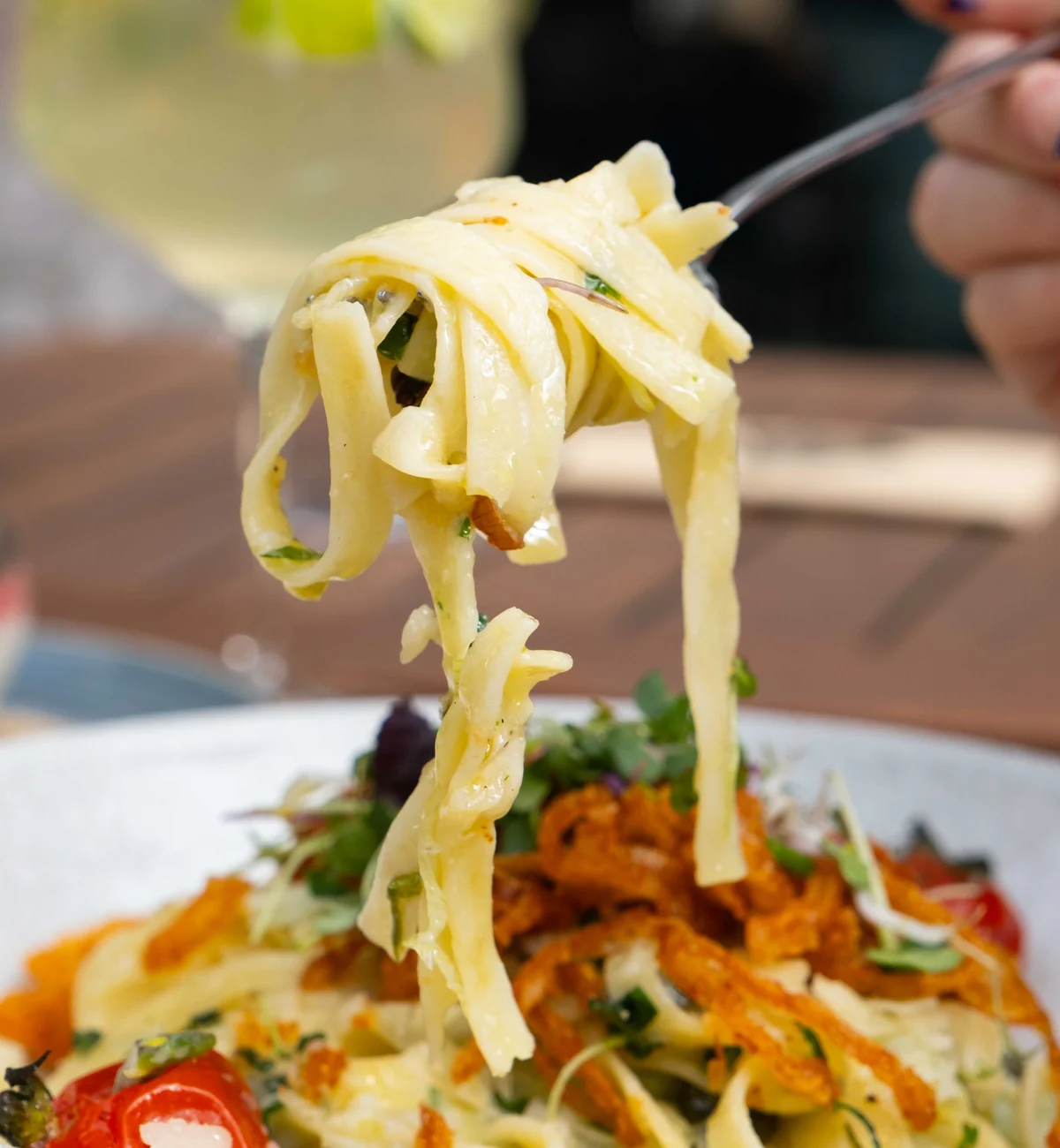 Gabel mit Bandnudeln über einem Teller Pasta mit Gemüse und Kräutern