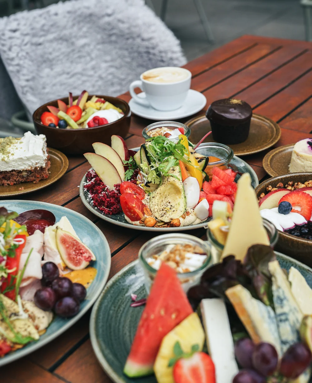 Frühstückstafel mit Obstteller, Käse, Aufschnitt, Bowls und Cappuccino auf der Terrasse