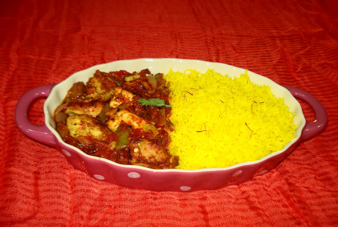 Chicken Tikka Masala in roter Currysauce neben Safranreis in einer ovalen Form