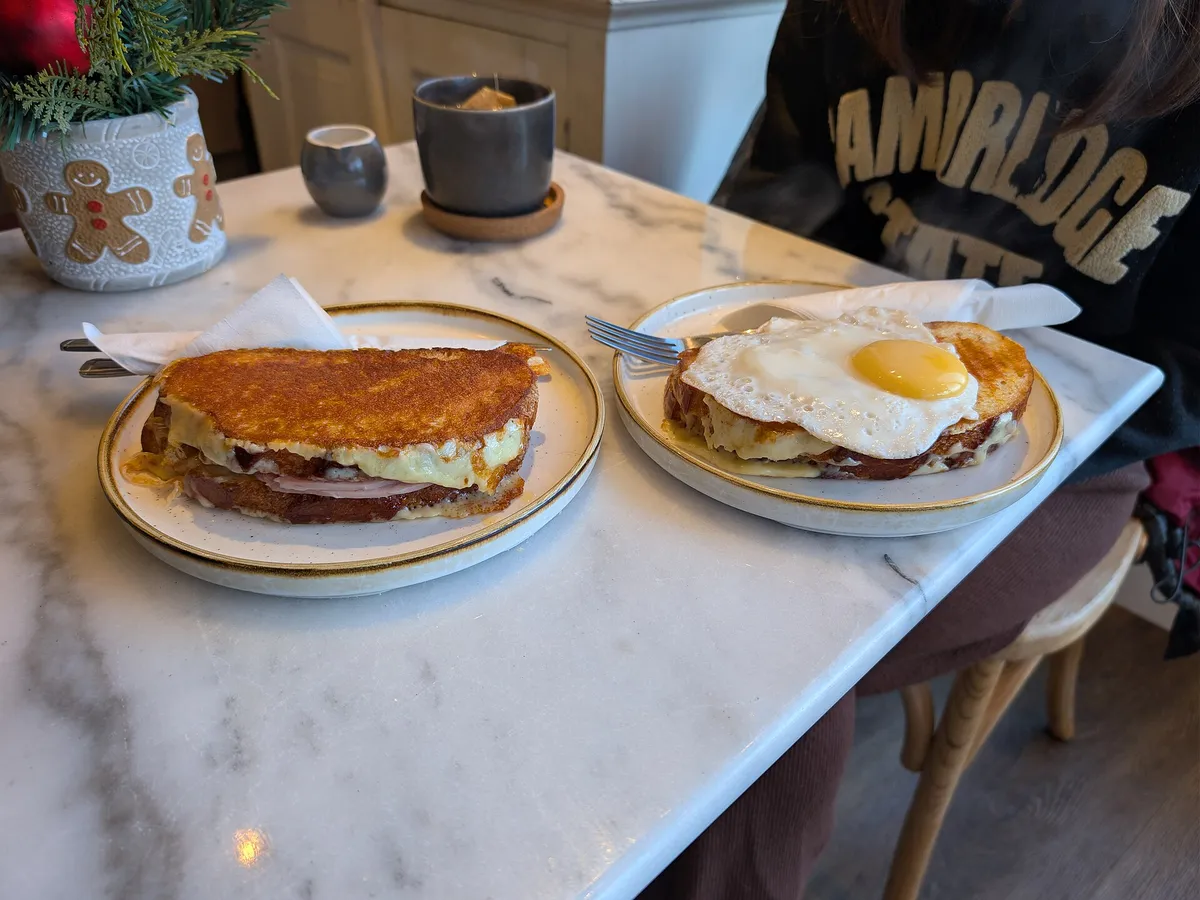 Croque Monsieur und Croque Madame mit Spiegelei auf zwei Tellern an einem Marmortisch